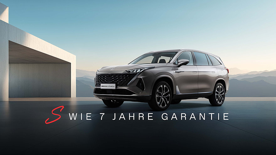 MGS9 PHEV in Camden Grey, Betonbau links, Berge im Hintergrund